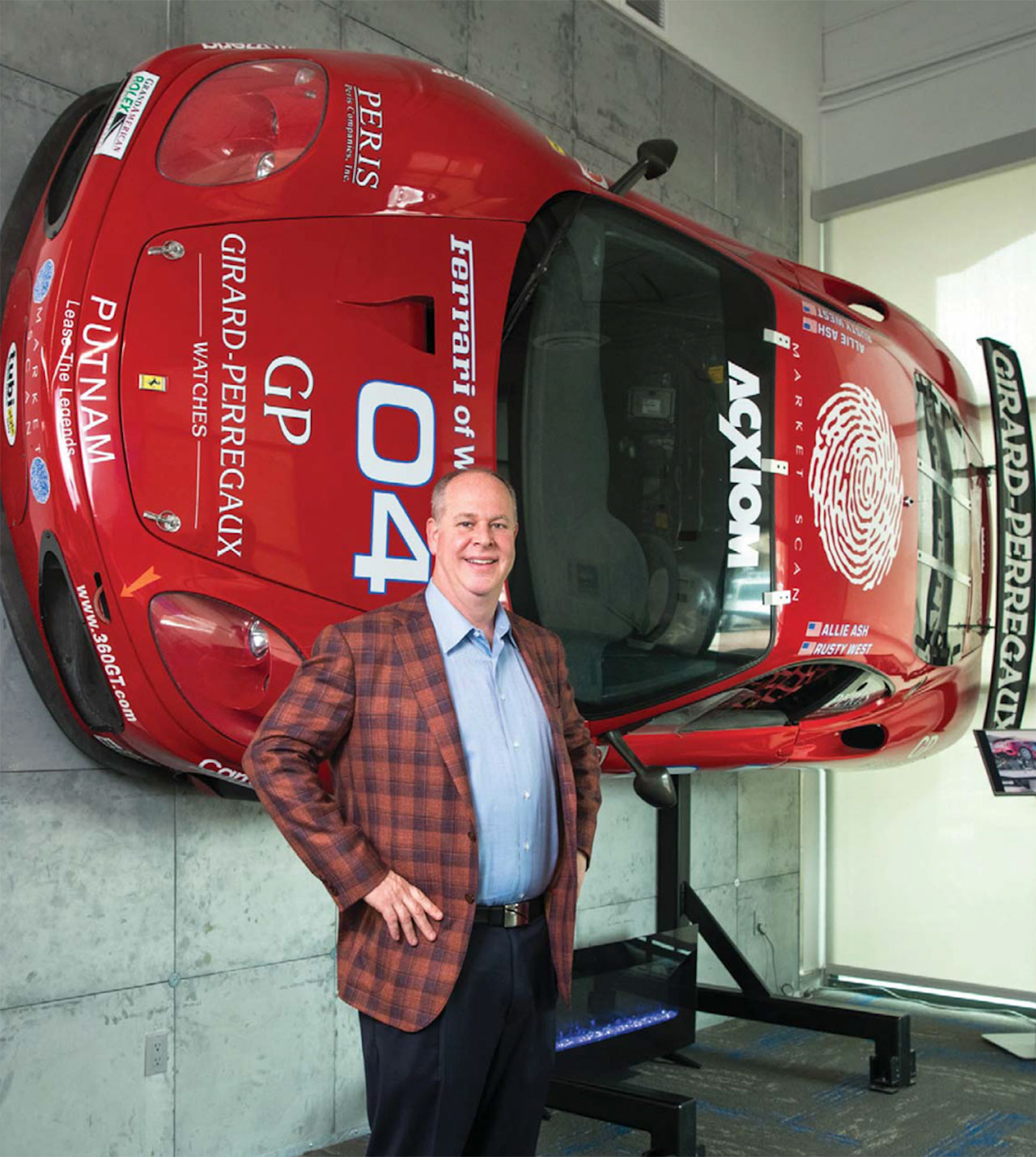 rusty-standing-in-front-of-wall-mounted-red-race-car Rusty West Standing in Front of Wall-Mounted Red Racecar